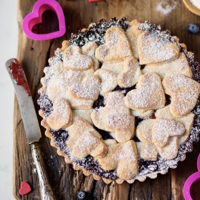 Tarte decorada com corações de massa e açúcar em pó sobre superfície de madeira