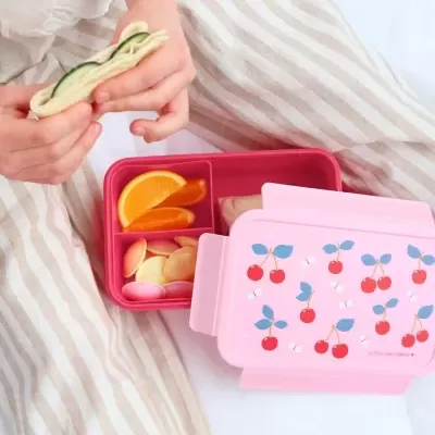 Marmita rosa com padrão de cerejas e comida com criança a segurar sandes enrolada