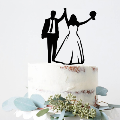 Bolo de casamento branco com figuras de noivos no topo e folhagens verdes na base.