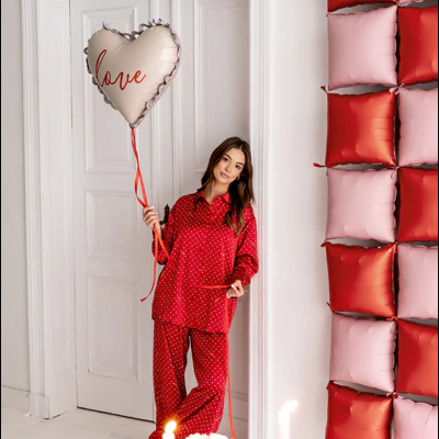 Mulher vestindo pijama vermelho segurando balão de coração com a palavra love