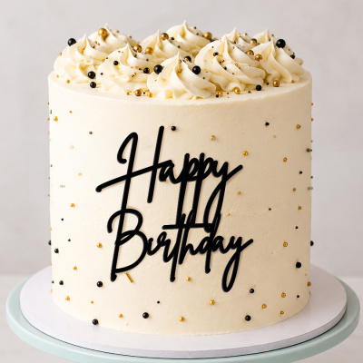 Bolo branco com decoração de pérolas douradas e pretas e texto Happy Birthday