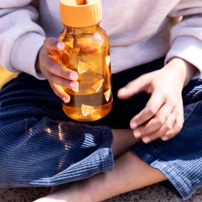 criança a segurar garrafa de plástico laranja sentada no chão