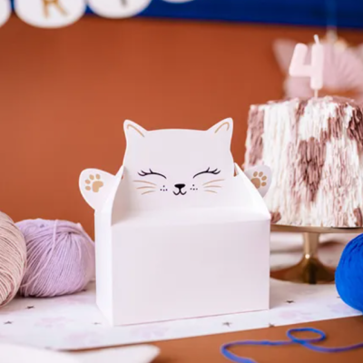 Cesto branco em forma de gato decorado com cara e patas desenhadas, ao lado de novelos de lã e bolo com número 4