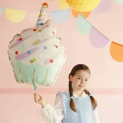 Criança com vestido azul aos quadrados segurando balão de cupcake numa festa com decorações coloridas