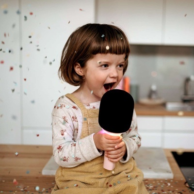 Criança segurando microfone rosa com luz na cozinha com confetes