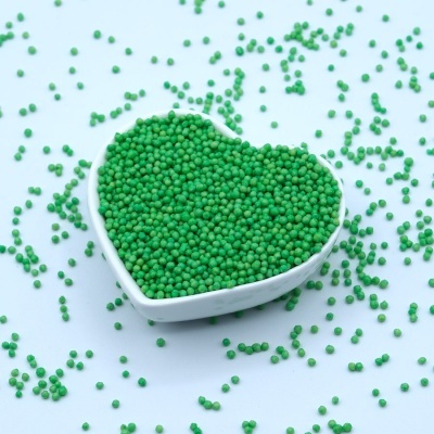 Taça branca em forma de coração cheia de esferas verdes com esferas espalhadas ao redor