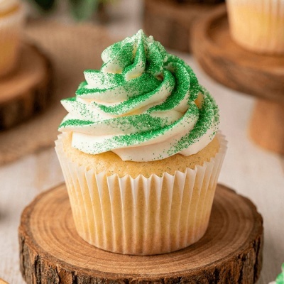Cupcake com cobertura branca e granulado verde em base de madeira.