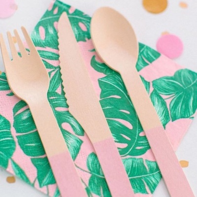 Talheres de madeira rosa sobre guardanapo com folhas verdes e confetes coloridos