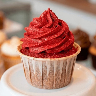 Cupcake com cobertura vermelha brilhante e base em papel branco num prato branco