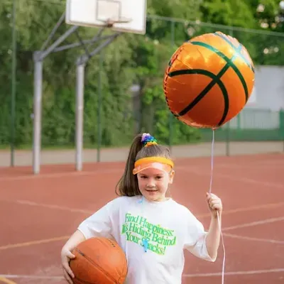 Menina com bola de basquetebol e balão laranja numa quadra de basquetebol ao ar livre