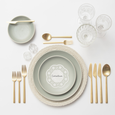 Conjunto de loiça e talheres dourados com copos e decoração rendada sobre mesa branca