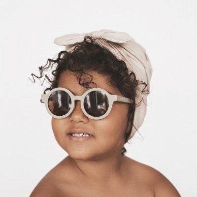 Criança com óculos de sol redondos brancos e lenço bege na cabeça