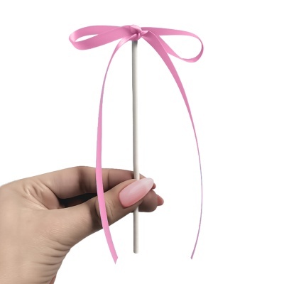 Vareta branca com laço rosa sendo segurada por mão com unhas pintadas de rosa claro