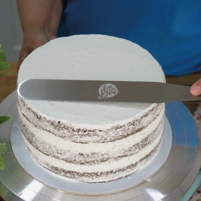 Bolo creme branco e bolacha numa base metálica com uma faca inscrita 'Just Love' a alisar o topo.