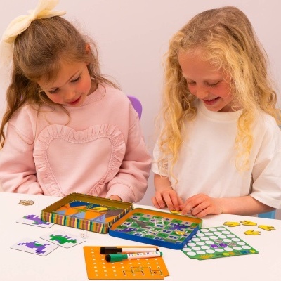 Duas meninas a jogar jogo de tabuleiro colorido com peças e cartas sobre mesa branca