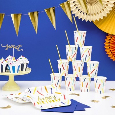 Conjunto de festa infantil com copos, pratos, guardanapos e cupcakes decorados, bandeirolas e elementos de papel coloridos num fundo azul