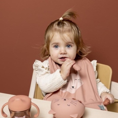 Bebé com babete rosa e acessórios de alimentação cor de rosa com motivos de gato.