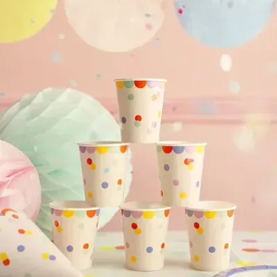 Copos de papel com padrão de pontos coloridos e decoração festiva ao fundo