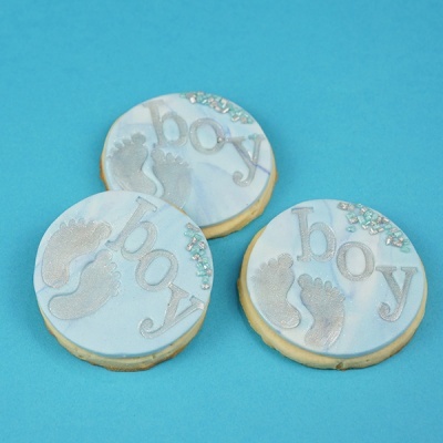 Três bolachas decoradas com tema de bebé menino sobre fundo azul.