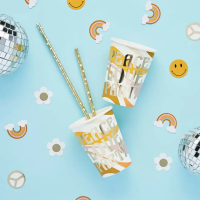 Dois copos de papel com canudos dourados e texto 'PEACE LOVE PARTY' em fundo azul com adesivos temáticos.