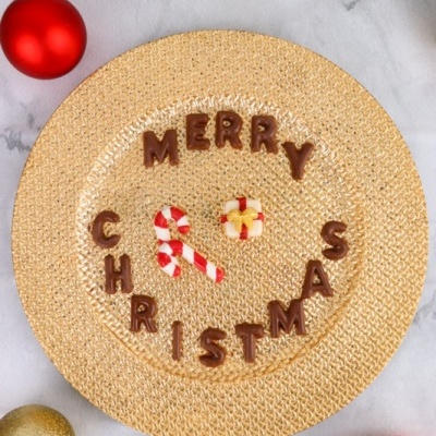 Prato decorativo de tecido dourado com tema de Natal e letras de chocolate.