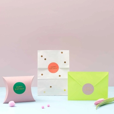 Três embalagens coloridas para aniversário com texto 'HAPPY BIRTHDAY' em fundo pastel