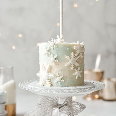 Bolo decorado com flocos de neve brancos e vela acesa num prato de vidro com fita rendada