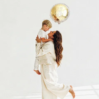 Mulher segurando criança com roupa branca e balão dourado com texto motivacional