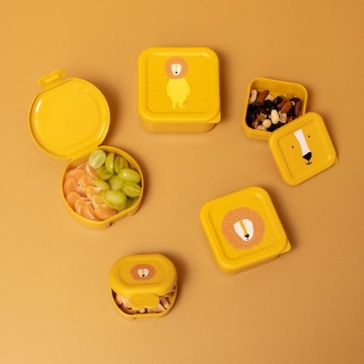 Cinco recipientes alimentares amarelos com desenhos de leão em tampas, com frutas e frutos secos, sobre fundo amarelo.