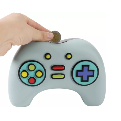 Mealheiro em forma de comando de videojogo cinzento com botões coloridos e mão a colocar moeda