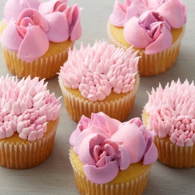 Cupcakes decorados com creme rosa em diferentes padrões sobre superfície cinzenta