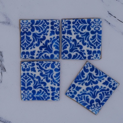Quatro azulejos quadrados de cerâmica azul e branco com padrão floral e arabesco