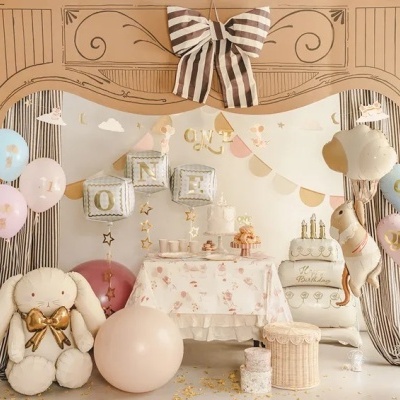 Decoração de festa de aniversário com balões coloridos, almofada coelho, mesa com bolo e cortinas às riscas.