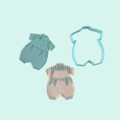 Molde plástico azul e duas decorações de macacão, azul e rosa, com detalhes, sobre fundo azul claro