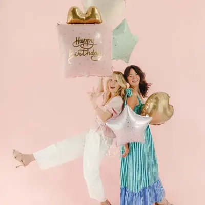 Duas mulheres com balões de aniversário coloridos em fundo cor-de-rosa