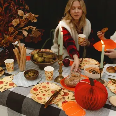 Mesa de jantar decorada com tema de outono com pratos e copos de papel, velas e decoração com abóboras e folhagem seca.