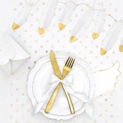 Mesa decorada com pratos brancos, talheres dourados com fita, penas brancas com pontas douradas e guardanapo em forma de asa