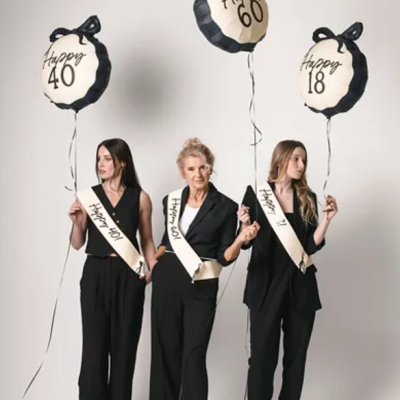 Três mulheres com balões e faixas de aniversário em fundo branco