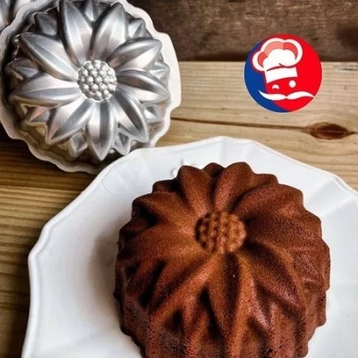 Forma metálica de bolo em forma de flor e bolo castanho moldado num prato branco sobre madeira