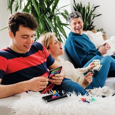 Pessoas a jogar jogo de tabuleiro com peças coloridas num sofá cinzento