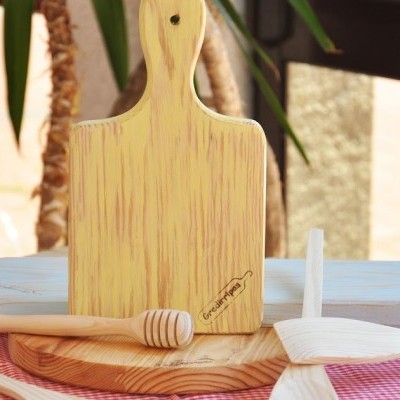 tabuleiro de madeira clara com alça e utensílios de cozinha de madeira sobre mesa com toalha rosa