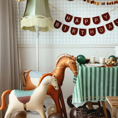 Decoração festa aniversário com balões, cavalos insufláveis, candeeiro e bolo numa mesa