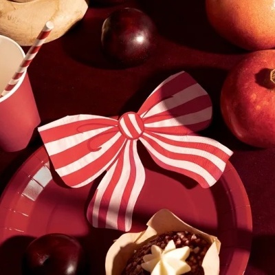 Conjunto de festa com copo e prato vermelhos, guardanapo riscado, frutas e vela acesa