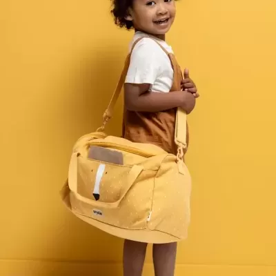Criança sorridente com saco amarelo e roupa casual num fundo amarelo.