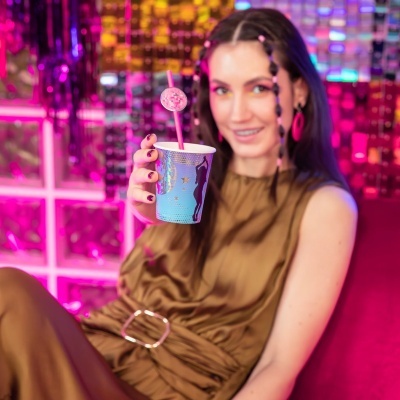 Mulher segurando copo azul com palhinha em ambiente festivo rosa