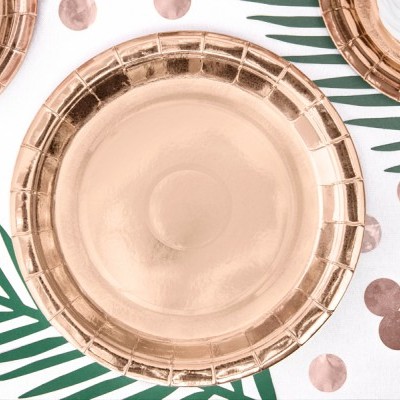 Pratos de papel metalizados cor de rosa dourado em toalha decorada com folhas verdes e confetes redondos.