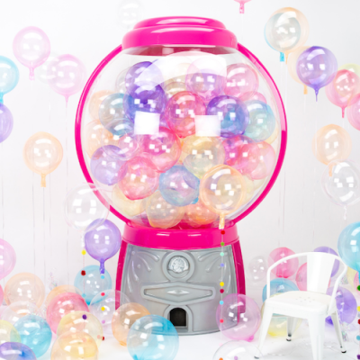 Máquina de bolas cor-de-rosa e cinzenta cheia de bolas coloridas, balões transparentes coloridos e cadeira branca