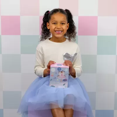 Criança com saia azul de tule e camisola bege segurando caixa de puzzle de bailarina