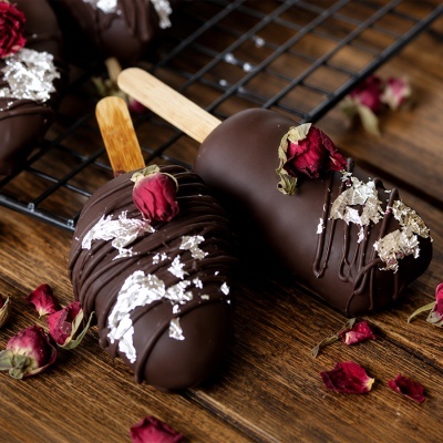 Dois gelados cobertos com chocolate preto decorados com flocos prateados e rosas secas