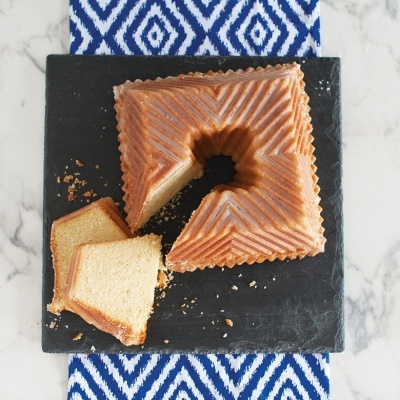 Bolo estriado quadrado com fatias servidas numa placa preta sobre tecido azul e branco